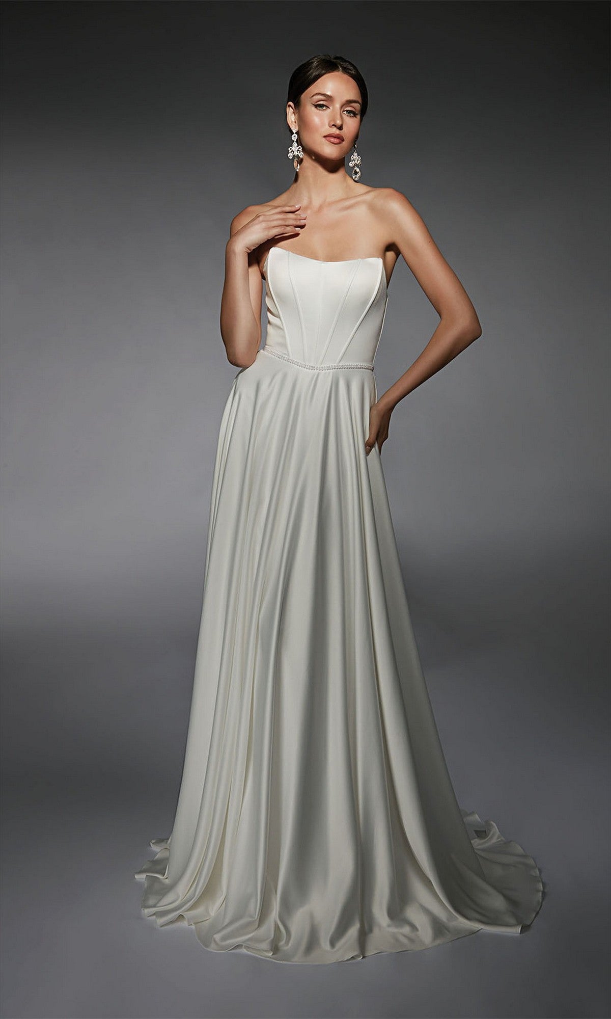 A woman poses elegantly against a dark background, wearing the Alyce 7110 Long White Dress—a strapless formal gown with a fitted bodice and flowing skirt.